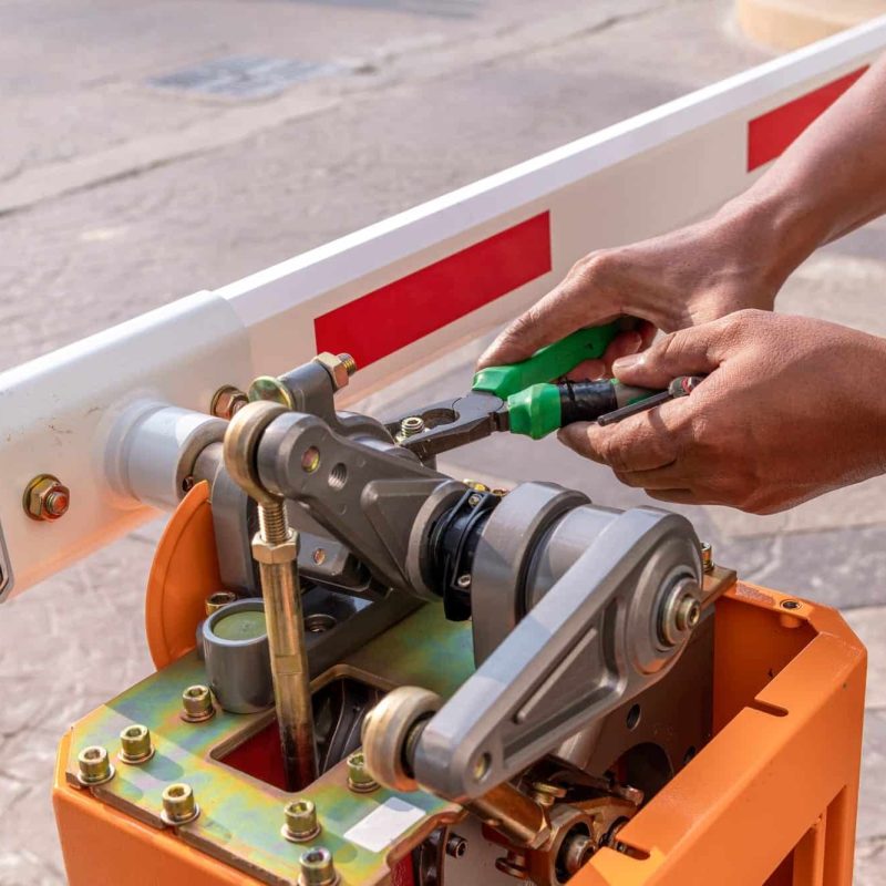Technician assembling automatic barrier gate system for entrance security. Close-up of barrier mechanism and hands using tools.